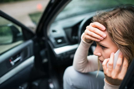 Young woman stressed out talking on the phone in the driver's seat of a compact car with the door open