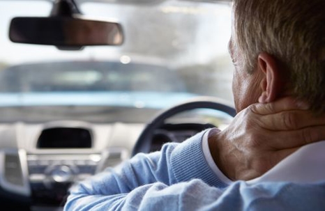 Man in the driver's seat of a car holding his neck
